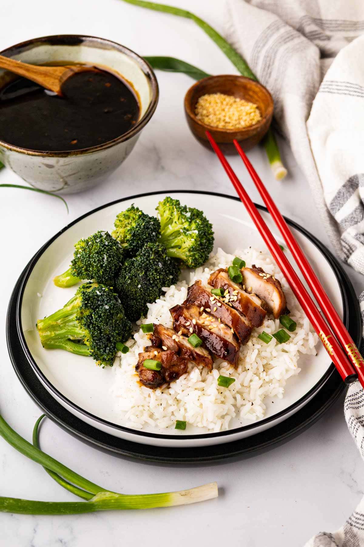 Sliced teriyaki chicken on top of white rice served with broccoli on a white plate.