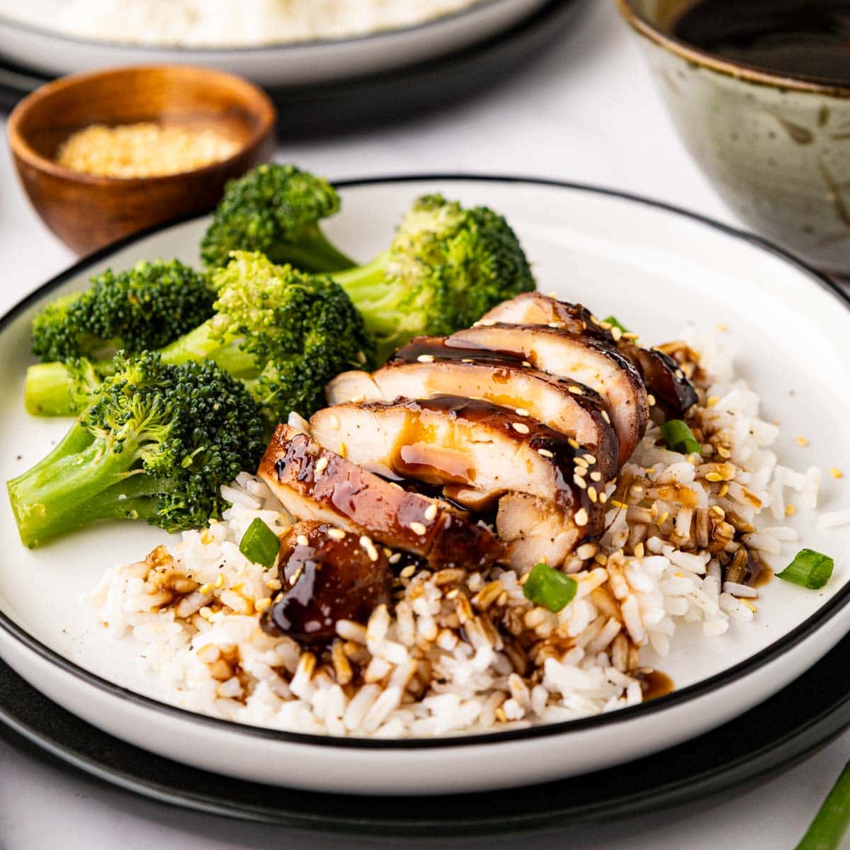 A white plate with teriyaki chicken, rice and broccoli with a teriyaki sauce glaze drizzled over the top.