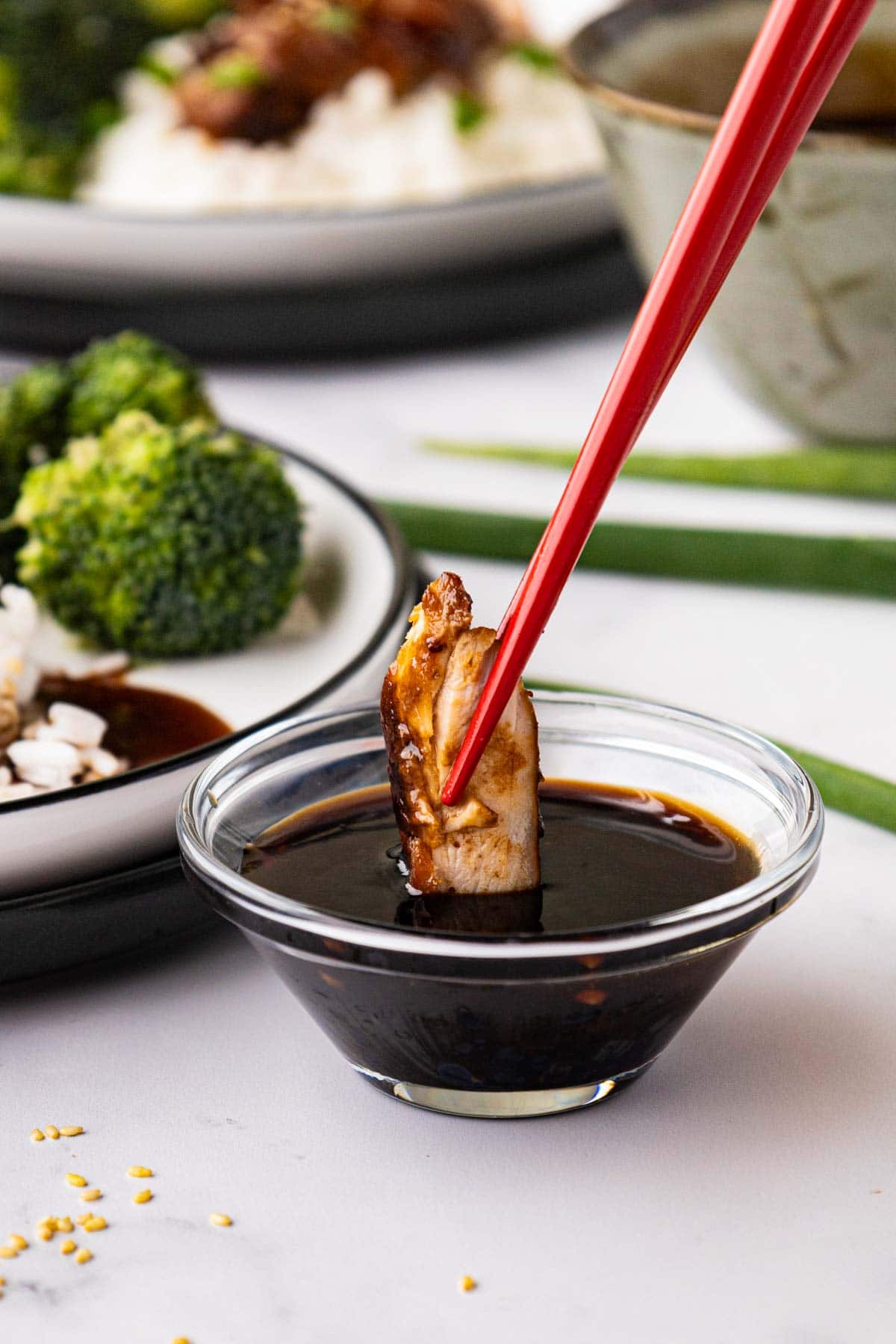 Using chopsticks to dip chicken into teriyaki sauce in a clear ramekin.