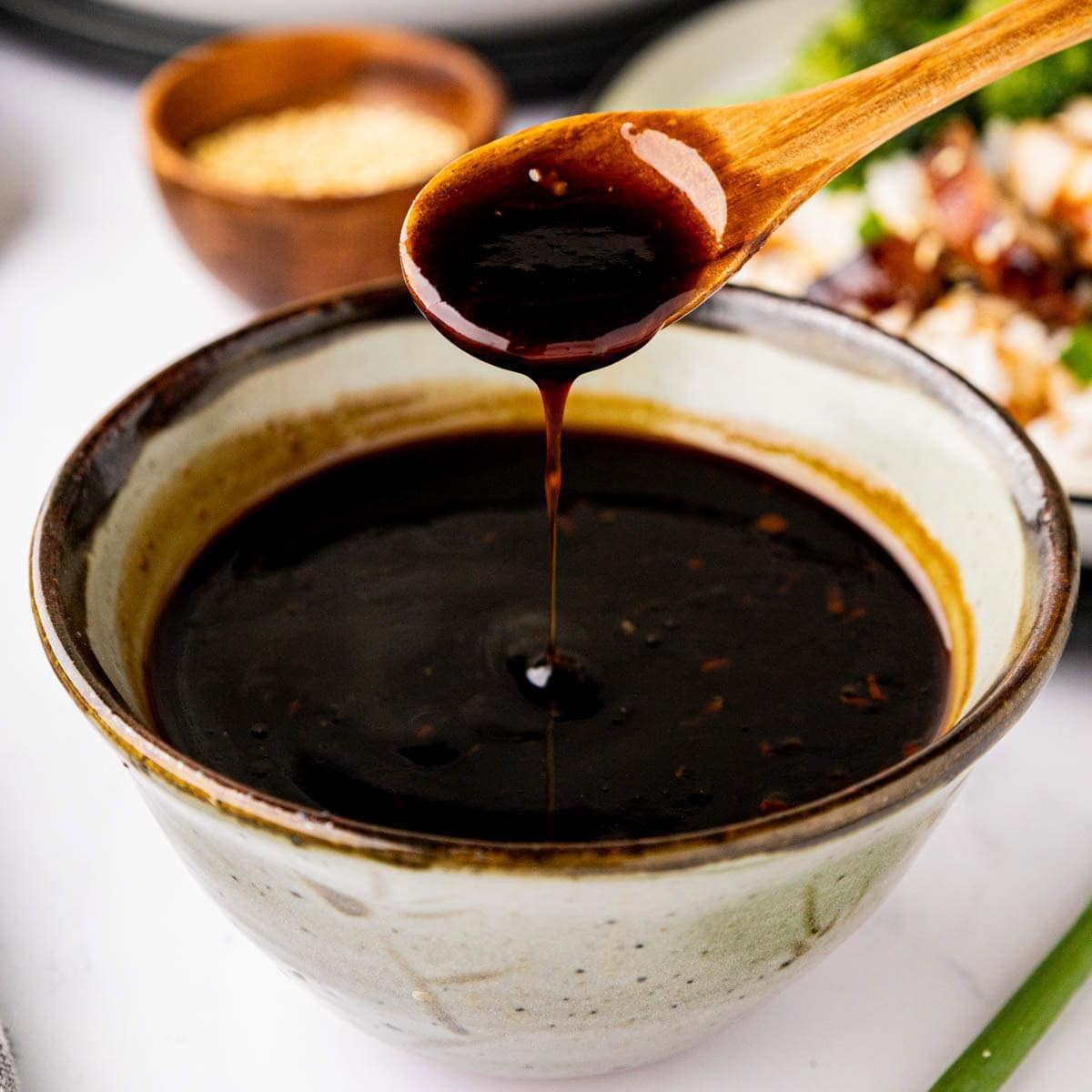 Teriyaki sauce in a bowl with a wooden spoon removing a scoop of sauce.