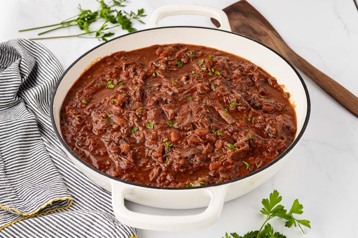 Beef ragu in a white dutch oven garnished with parsley.