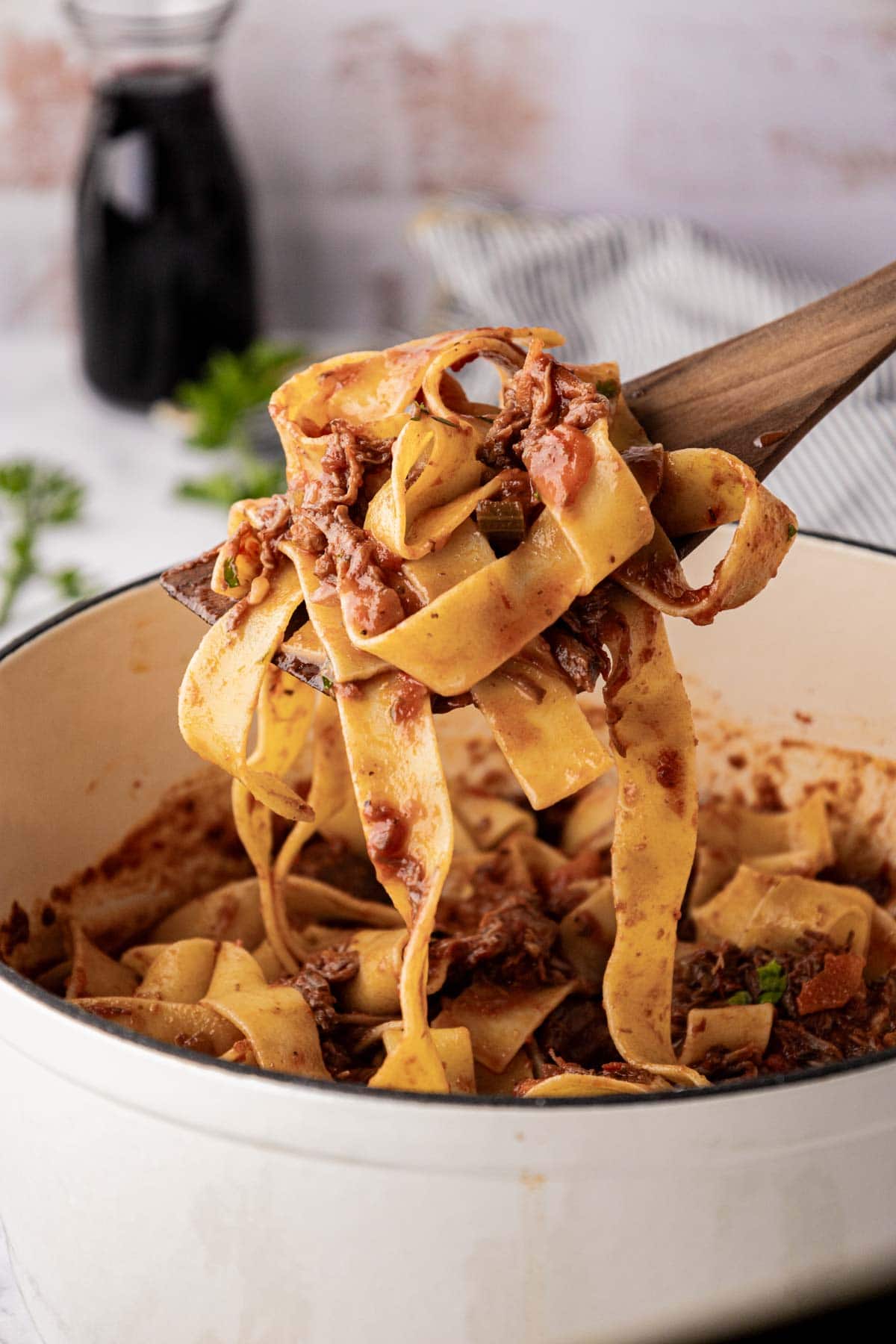 Beef ragu with pappardelle swirled on a wooden spoon.