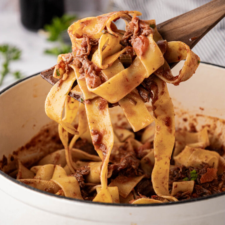 Beef ragu with pappardelle pasta swirled on a wooden spoon.