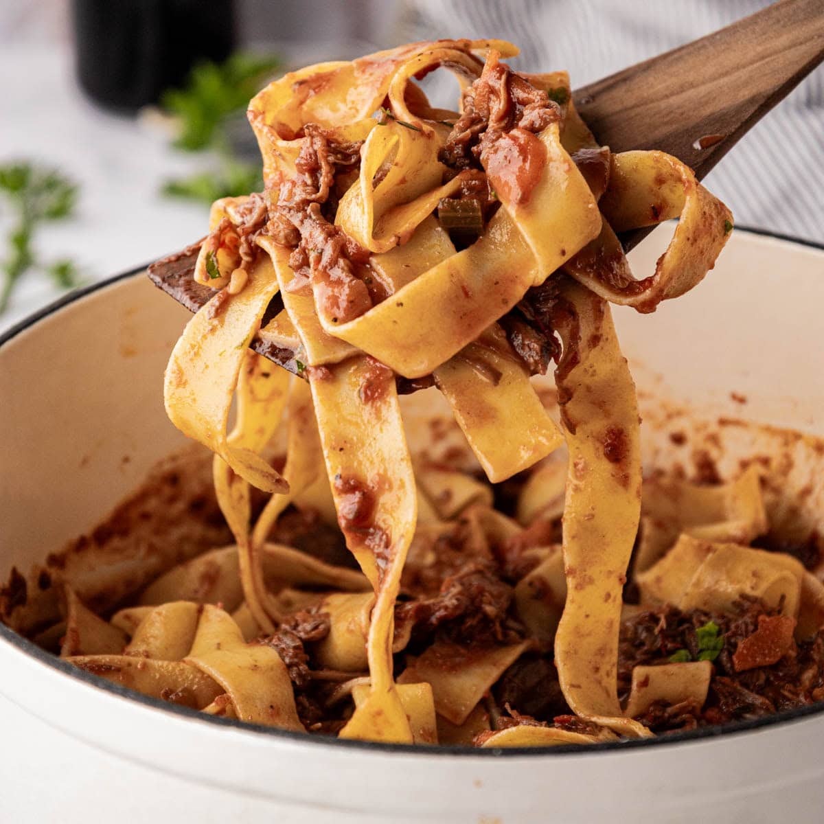Beef ragu with pappardelle pasta swirled on a wooden spoon.