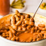 A ladle scooping out bloody mary boiled peanuts from a pot.