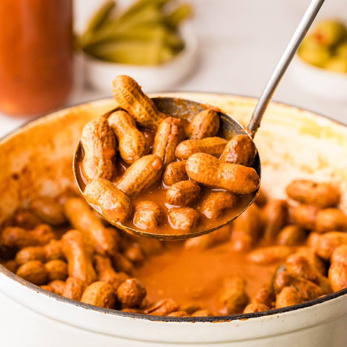 A ladle scooping out bloody mary boiled peanuts from a pot.