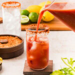Pouring a bloody mary into a glass with bloody mary rim salt.