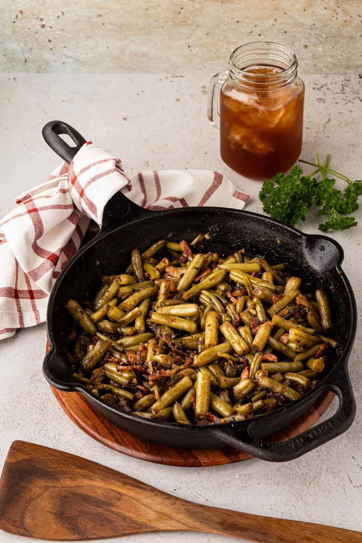 Bacon brown sugar green beans with soy sauce served in a cast iron skillet with a glass of iced tea.