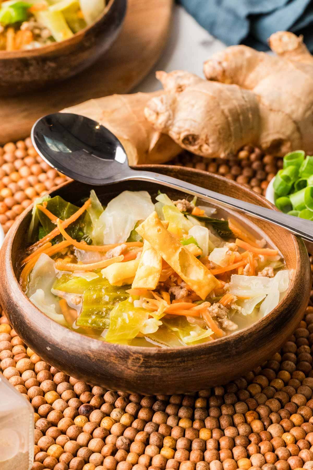 Wooden bowl filled with egg roll soup with a spoon on the edge of the bowl.