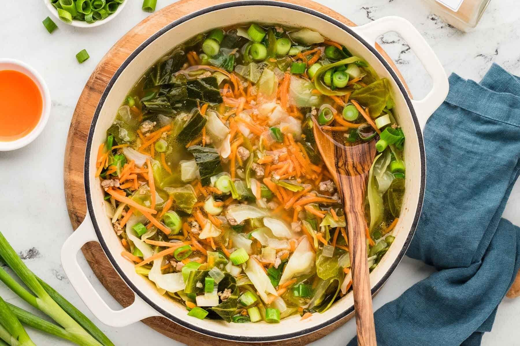 Overhead shot of egg roll soup in a large pot with a wooden spoon.