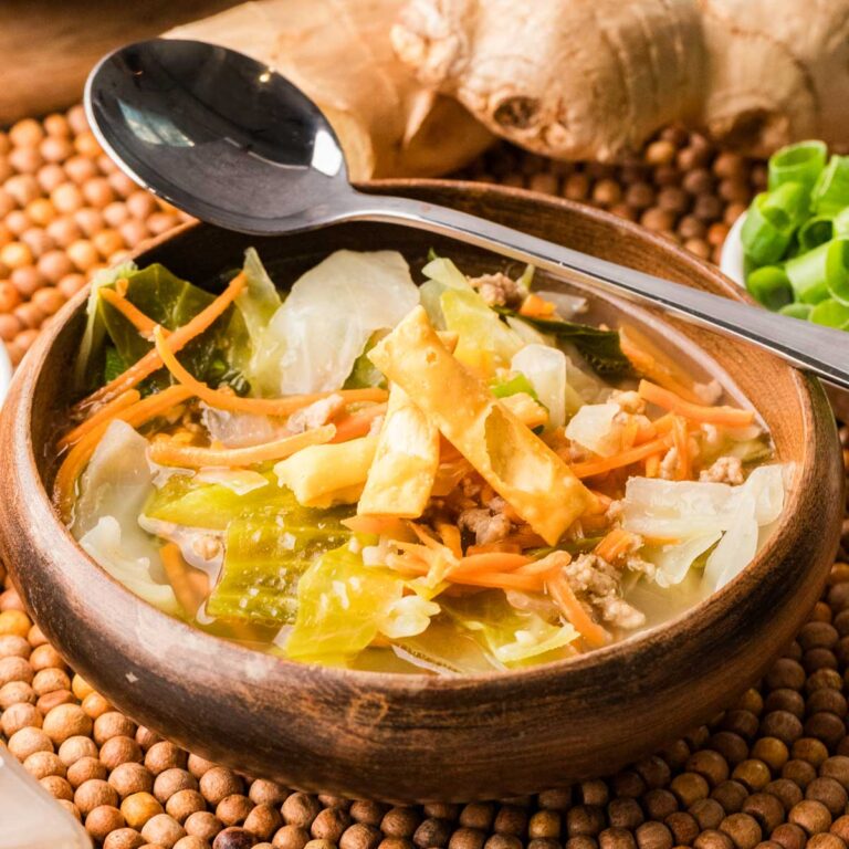 Bowl of egg roll soup with wonton strips on top and the spoon on the edge of the bowl.