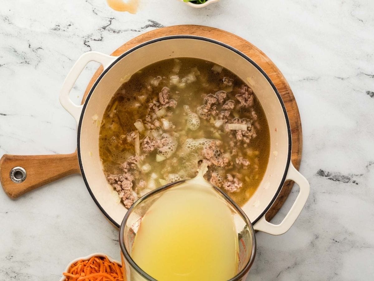 Broth being poured into the pot with the ground pork, onions and garlic.