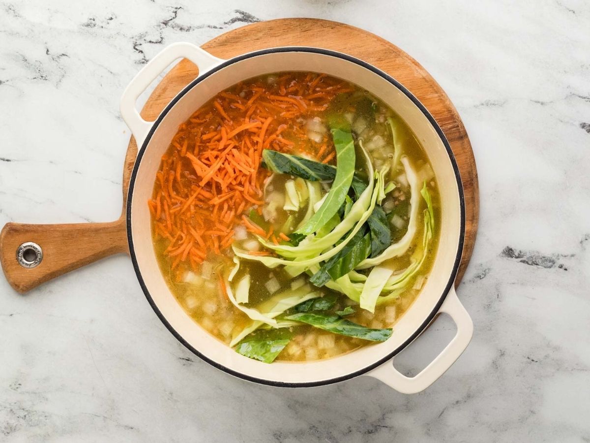 Vegetables added to the egg roll soup in a large pot.