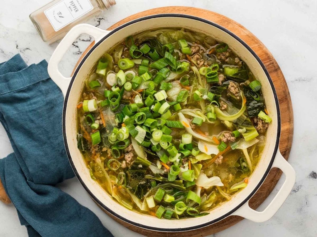 Green onions added to the egg roll soup in a large pot.