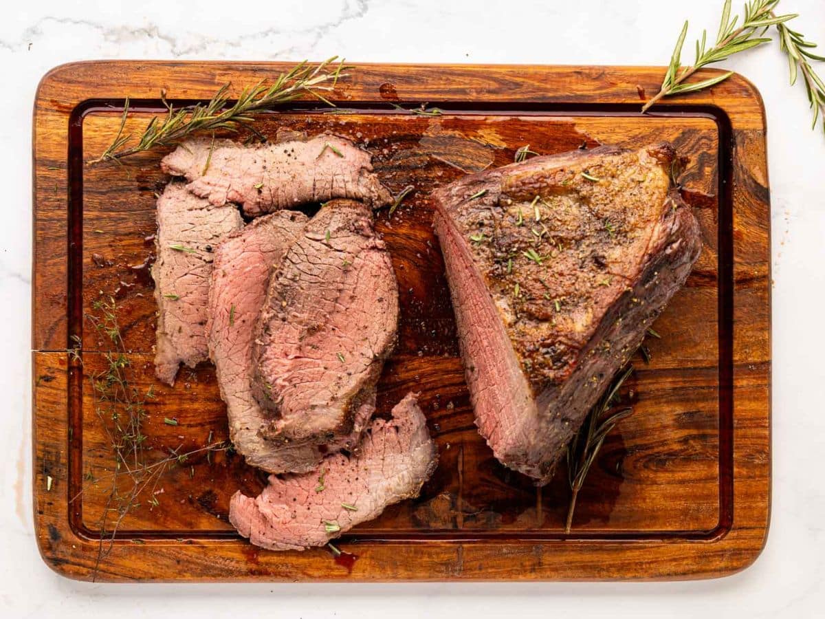 A sliced garlic herb rump roast on a wooden cutting board.