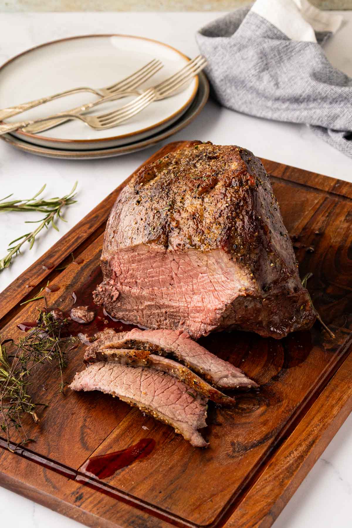 A sliced garlic herb roast beef on a wooden cutting board.