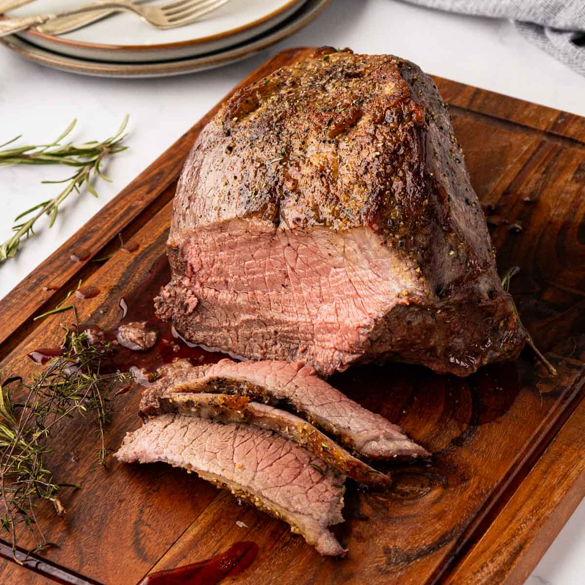 A sliced garlic herb roast beef on a wooden cutting board.