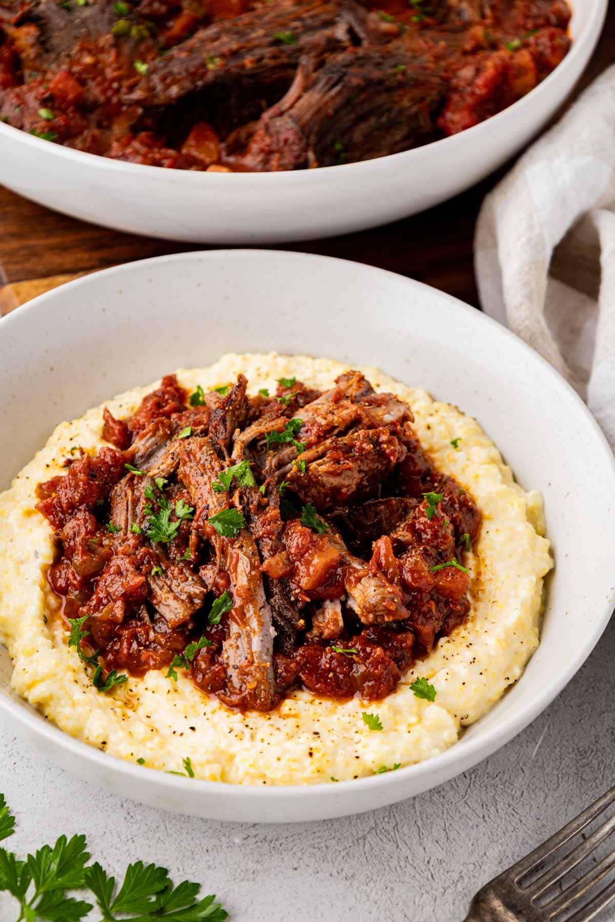 Shredded Italian pot roast served in a bowl on a bed of polenta.