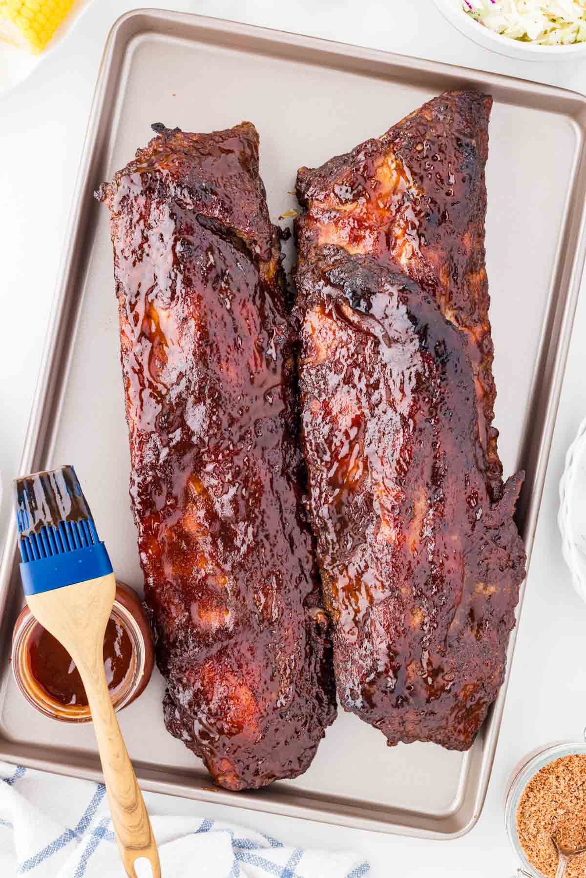 Oven baked ribs on a baking sheet with a basting brush and barbecue sauce set to the side