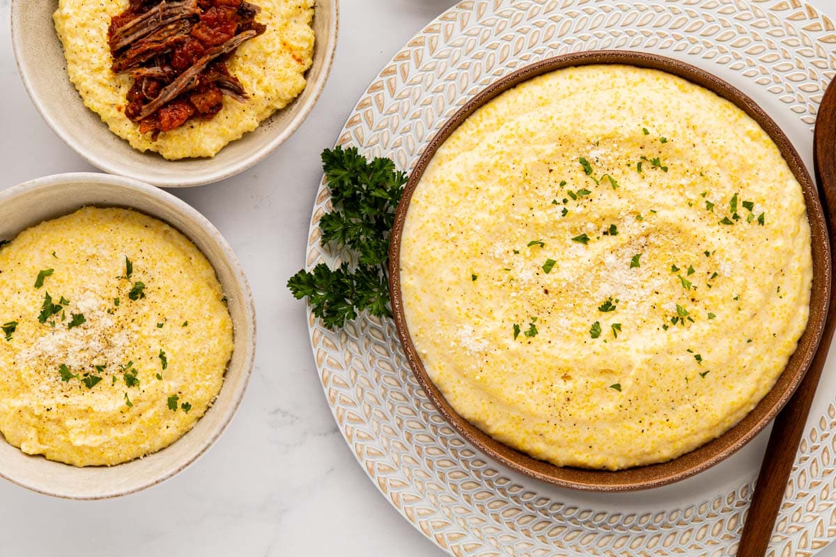 Overhead shot of polenta served in a serving bowl next to two bowls of polenta.