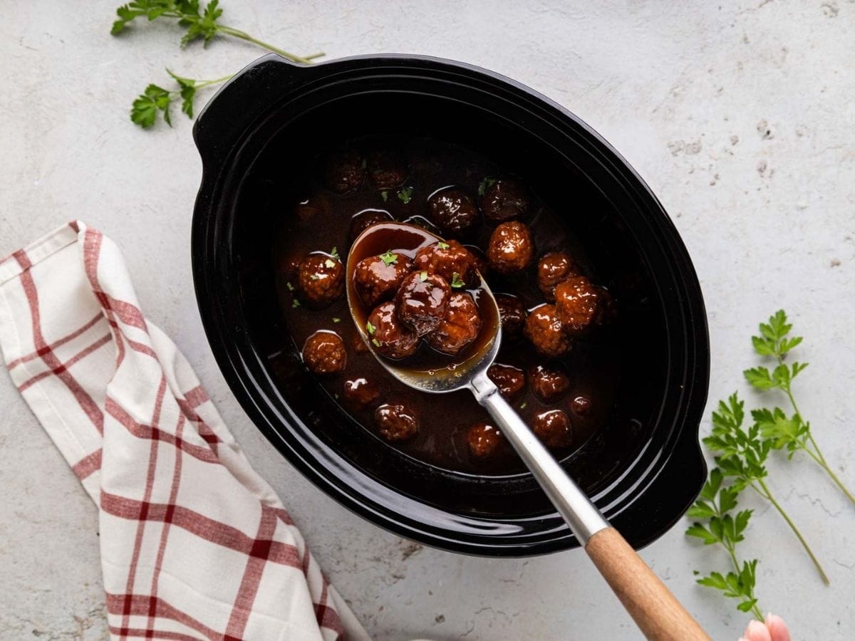 A serving spoons removing a scoop of pepper jelly meatballs.