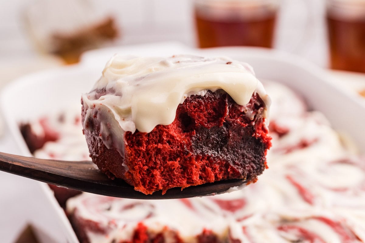 A wooden spatula removing a red velvet cinnamon bun from the baking dish.