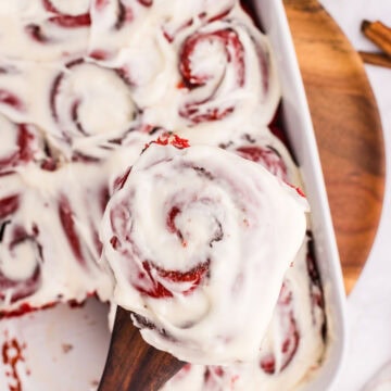 A wooden spatula removing a red velvet cinnamon bun from the baking dish.