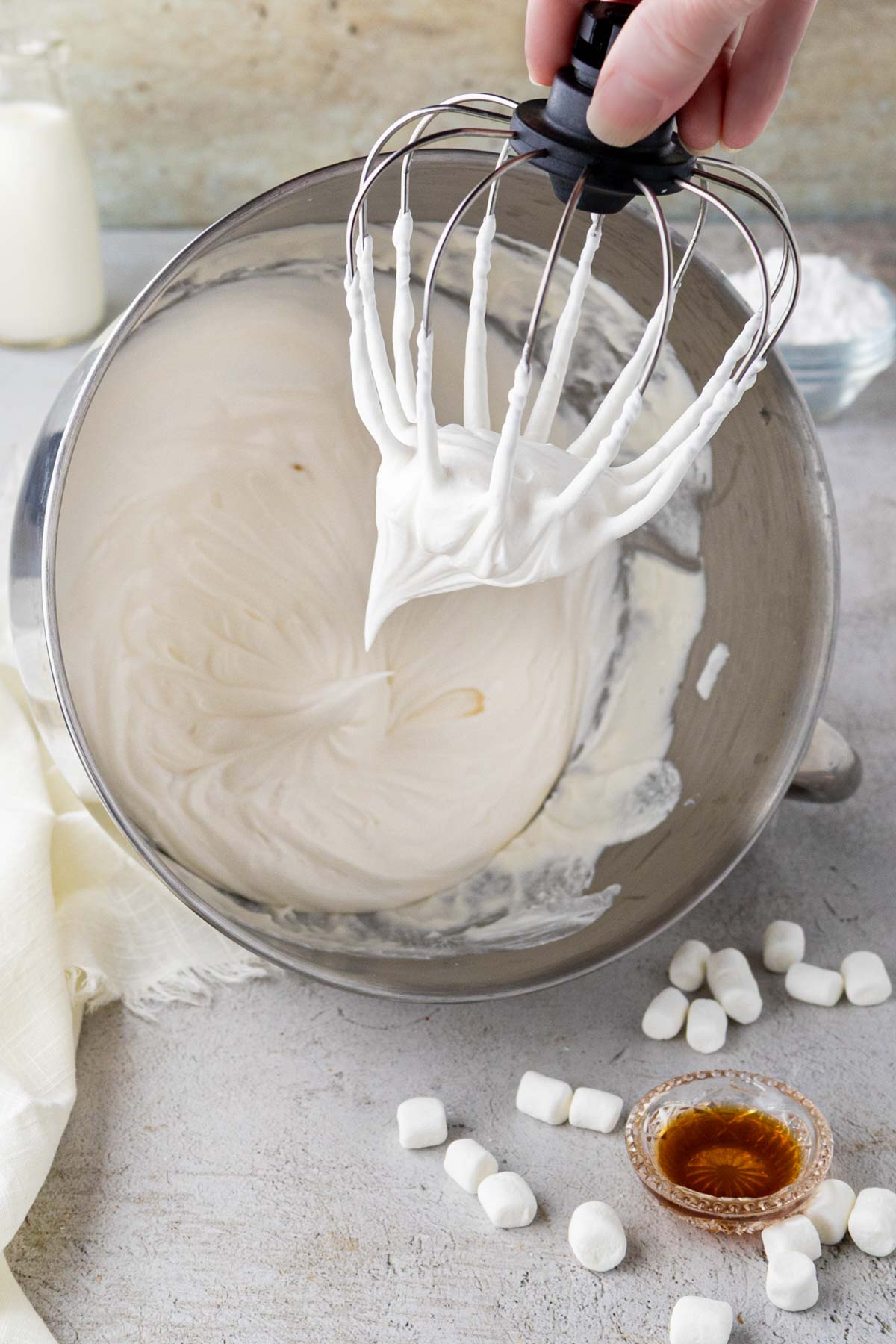 Marshmallow whippped cream in a bowl of a stand mixer with the whisk being removed.