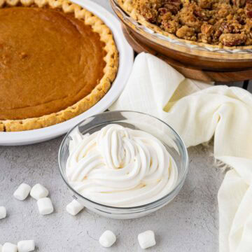Marshmallow whipped cream piped into a glass bowl with sweet potato pie in the background.