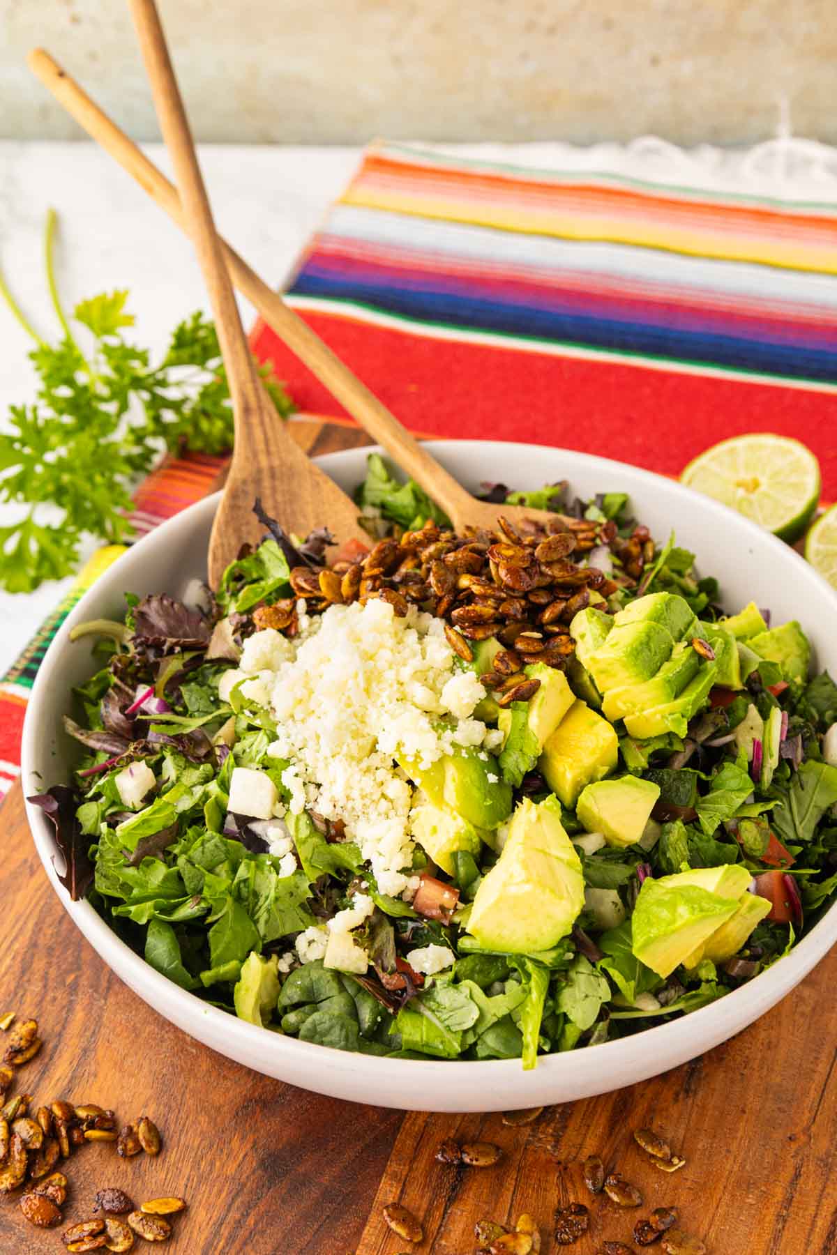 A Mexican chop salad and a white salad bowl with wooden serving spoons.