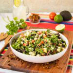A Mexican chop salad in a white bowl on a wooden board.