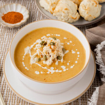 Pumpkin crab bisque garnished with lump crab pepitas, and a drizzle of heavy cream in a white bowl.