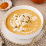 Pumpkin crab bisque garnished with lump crab pepitas, and a drizzle of heavy cream in a white bowl.
