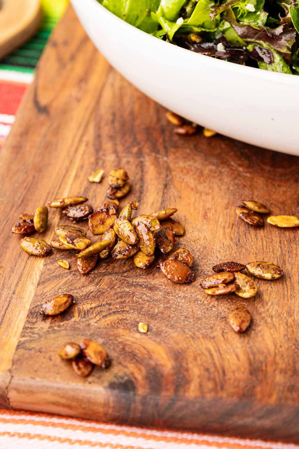 Spicy pepitas on a wooden board in front of a salad.