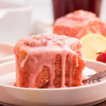 Side view of a strawberry cinnamon bun on a white plate.