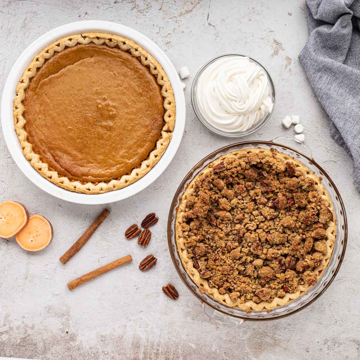 Two sweet potato pies on a table, one with pecan topping and one without.