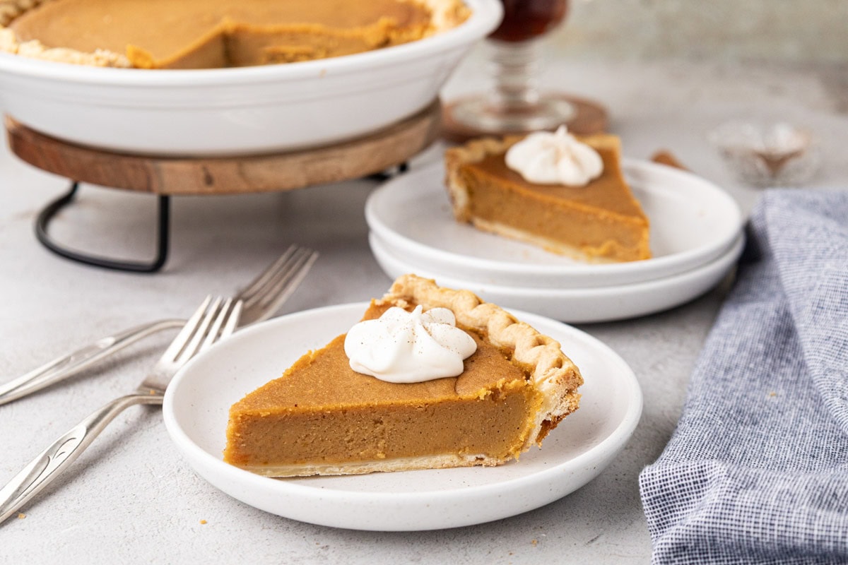 A slice classic sweet potato pie with a dollop of whipped cream and the whole pie in the background.