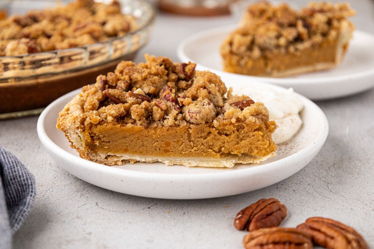 A spice of sweet potato pie with pecan topping on a white plate with a dollop whipped cream.