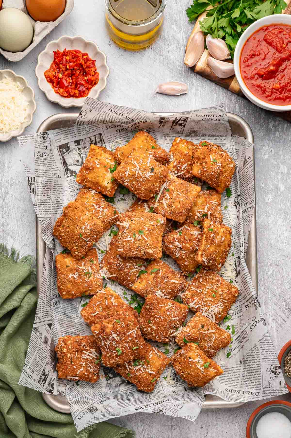 Overhead shot of toasted ravioli on a sheet pan next to marinara sauce.
