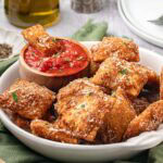 Fried ravioli served in a bowl with a side of marinara sauce.
