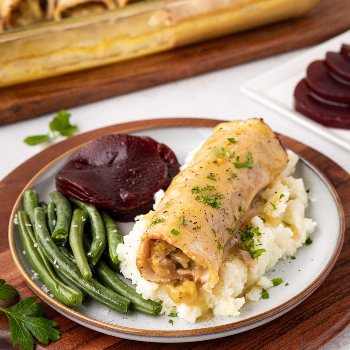 A turkey and stuffing roll up, served over mashed potatoes with green beans and cranberry sauce.