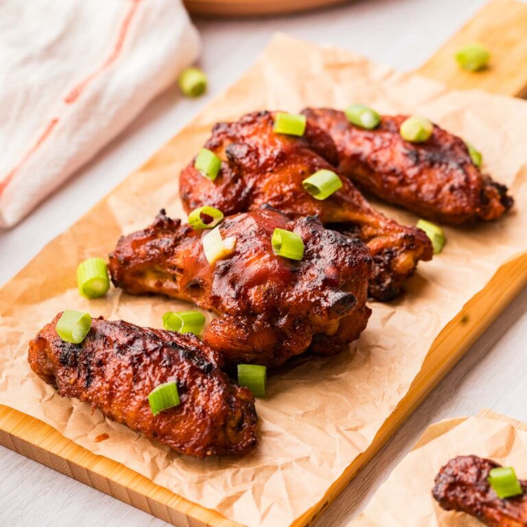 Air fryer BBQ chicken wings served on a wooden board lined with parchment paper.