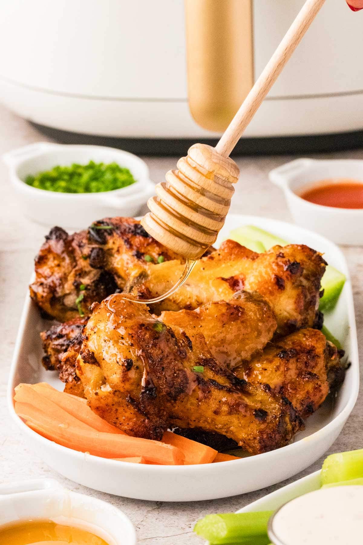 Drizzling honey on top of the hot honey chicken wings on a platter.