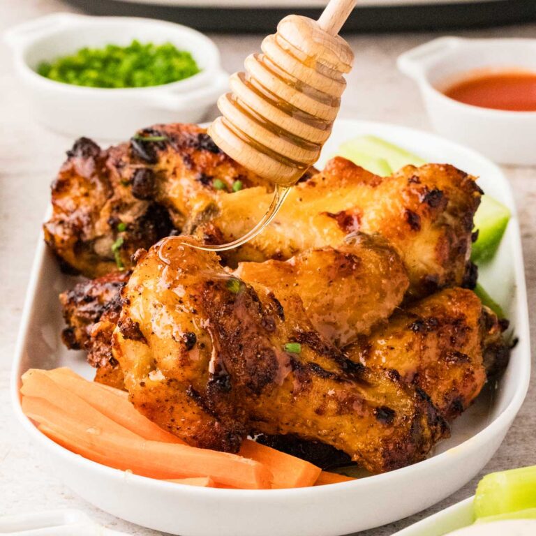 Air fryer hot honey chicken wings served on a platter with honey being drizzled on top.