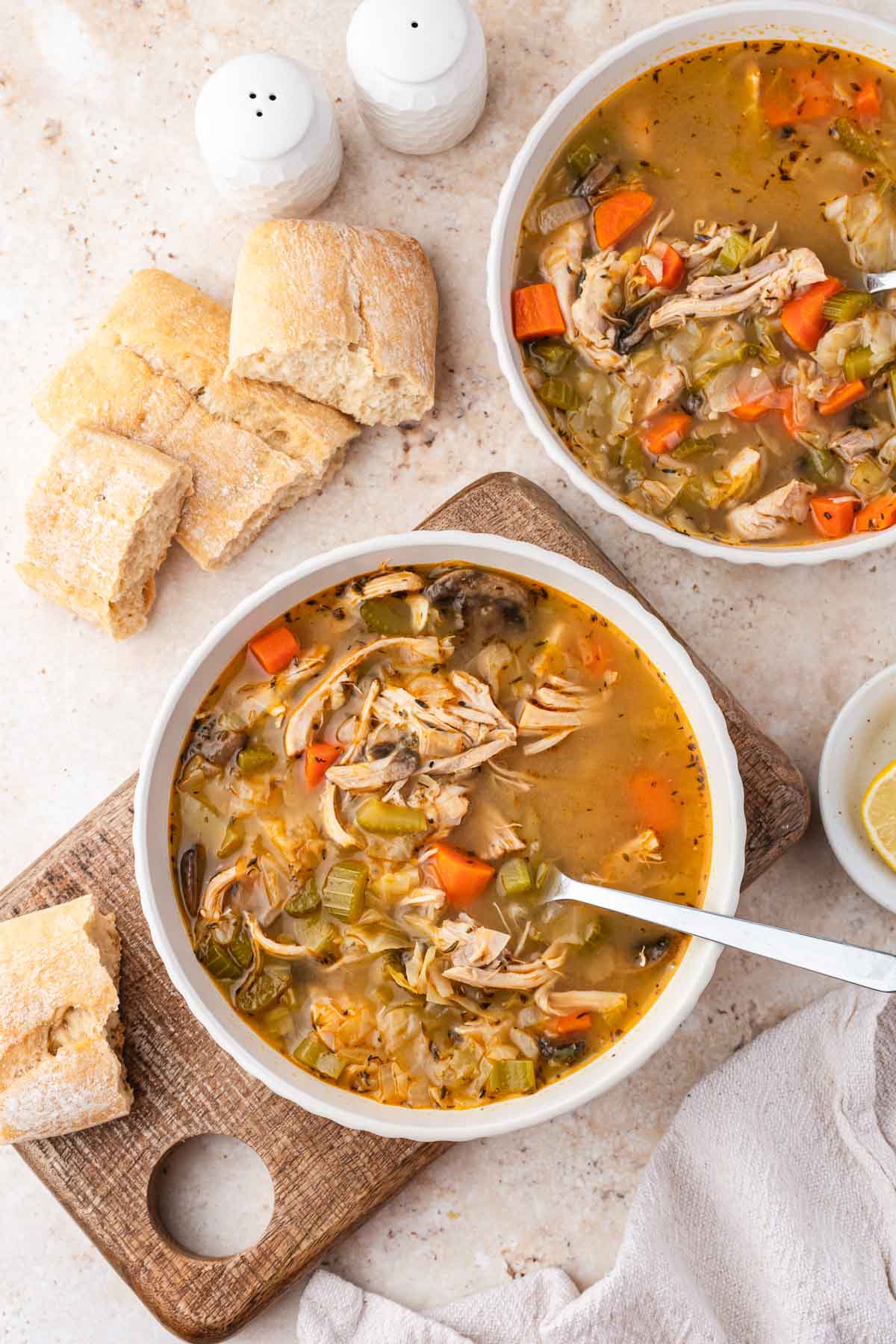 Overhead shot of two bowls of chicken cabbage soup with bread on the side.