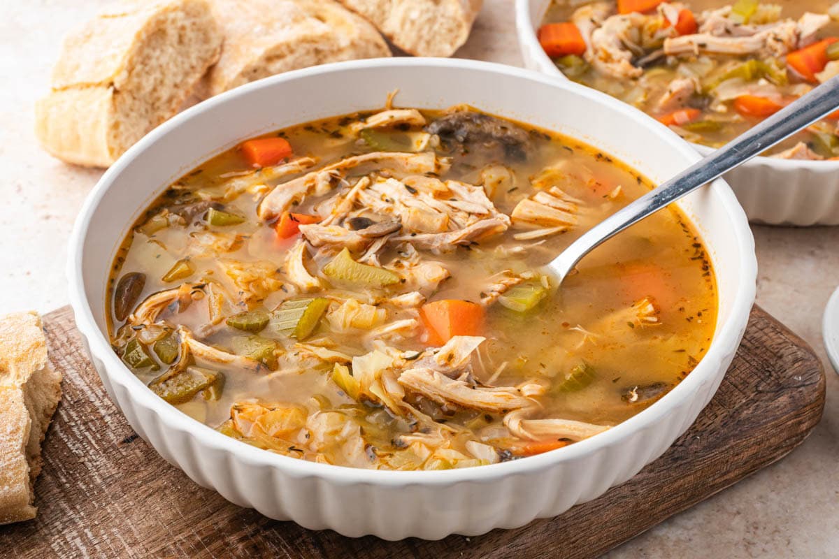 Large white bowl of chicken cabbage soup with a spoon in it on a wooden board.