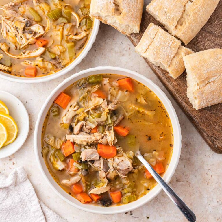 Overhead shot of chicken cabbage soup in a white bowl with bread on a wooden board.