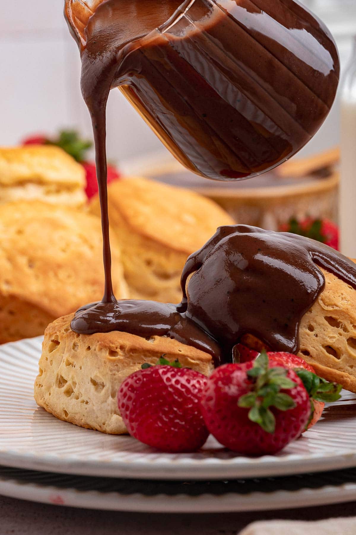 Side view of pouring chocolate gravy over the top of two biscuits.
