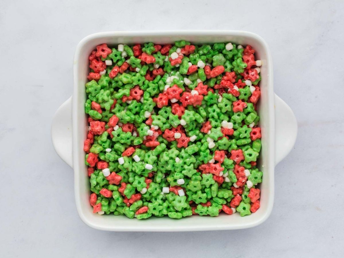 Pressing the cereal and marshmallow mixture into a baking dish.