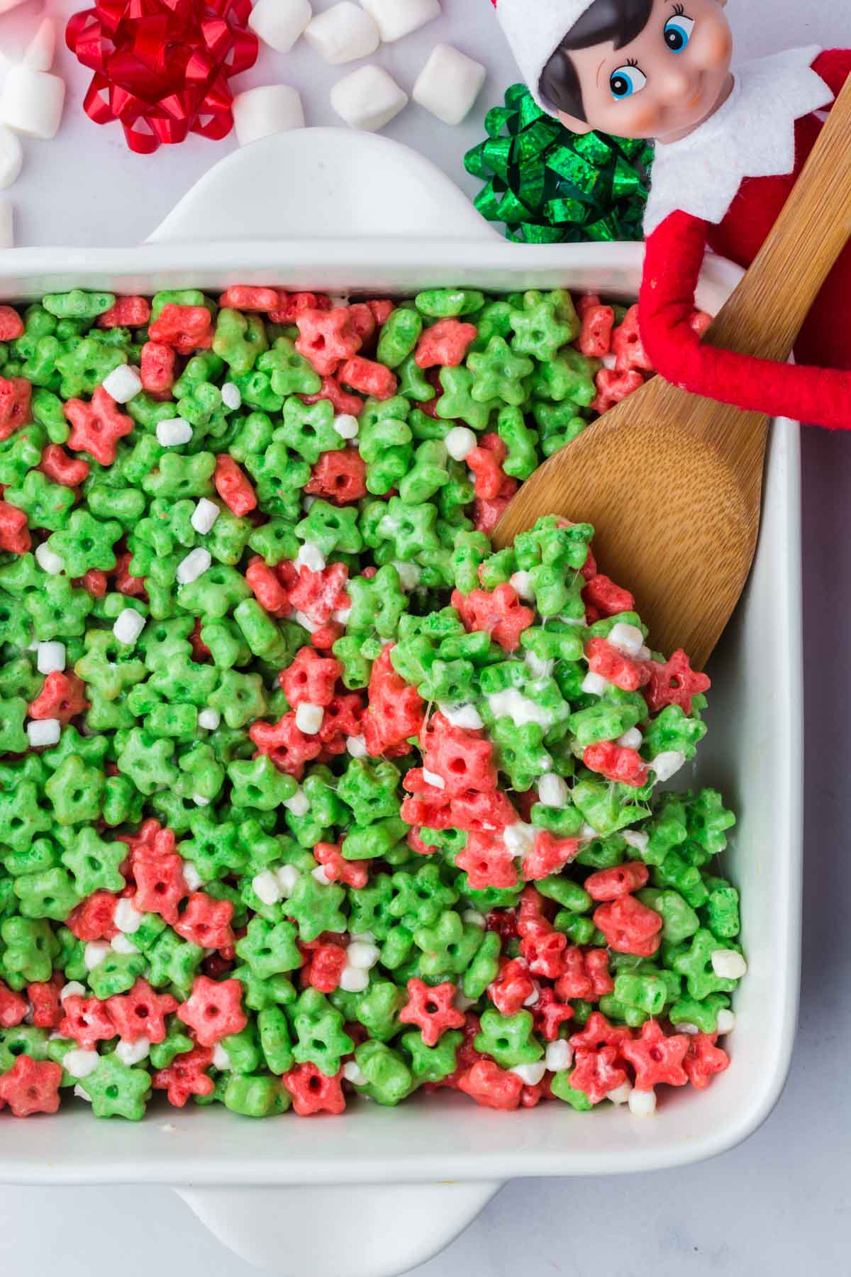 Elf on a shelf cereal treats in a baking dish with a wooden spoon scooping one up.
